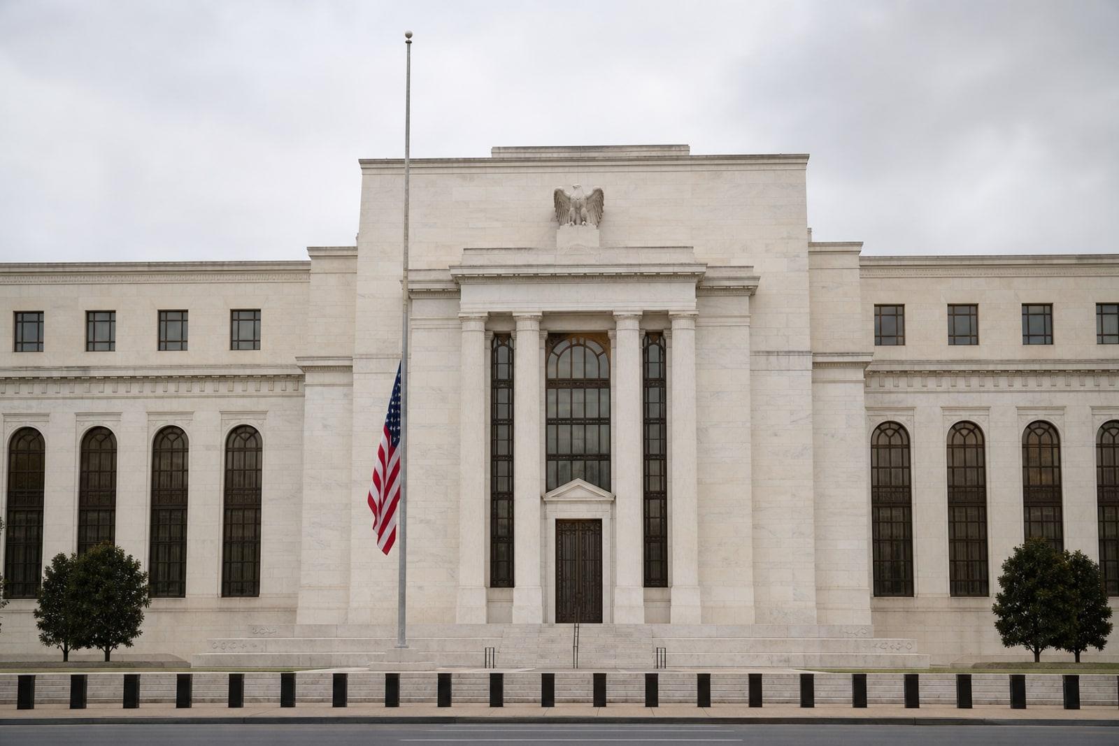 The marble facade of the Federal Reserve's Eccles Building in Washington under overcast light, with a US flag at half-staff.