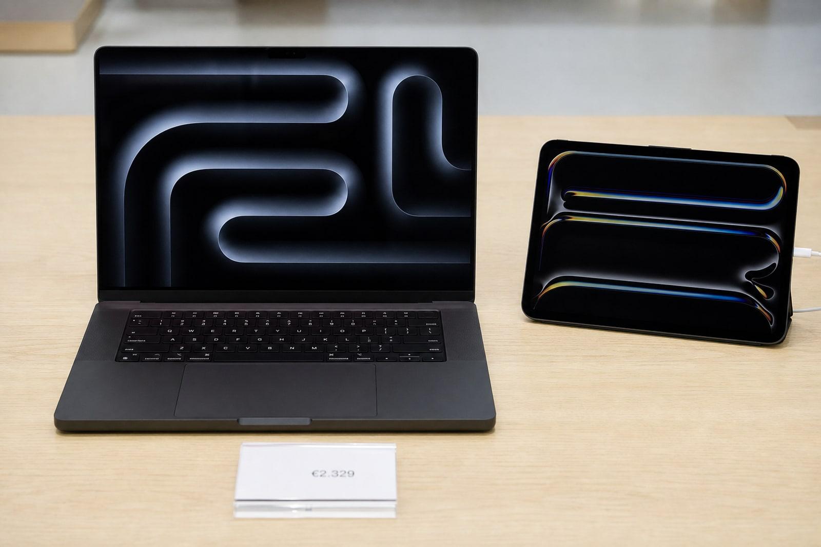 An Apple MacBook Pro and iPad Pro displayed on a pale-wood store table with a euro price card.