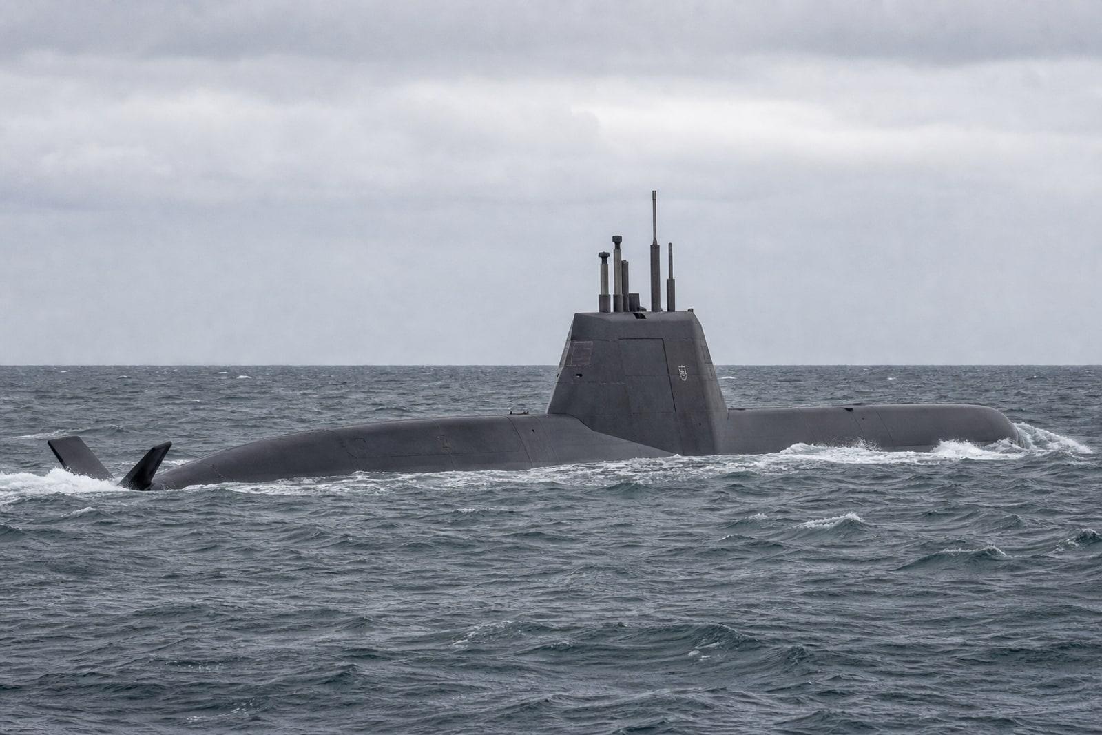 A TKMS Type 212CD conventional submarine with an angular stealth sail surfacing in grey North Atlantic water under an overcast sky.
