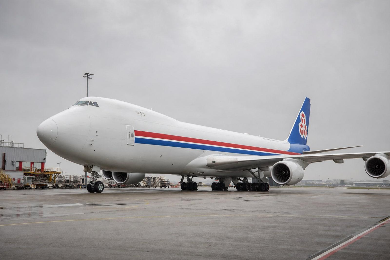A white Cargolux Boeing 747-8 freighter with red-and-blue livery stripes parked on an airport apron under grey skies.