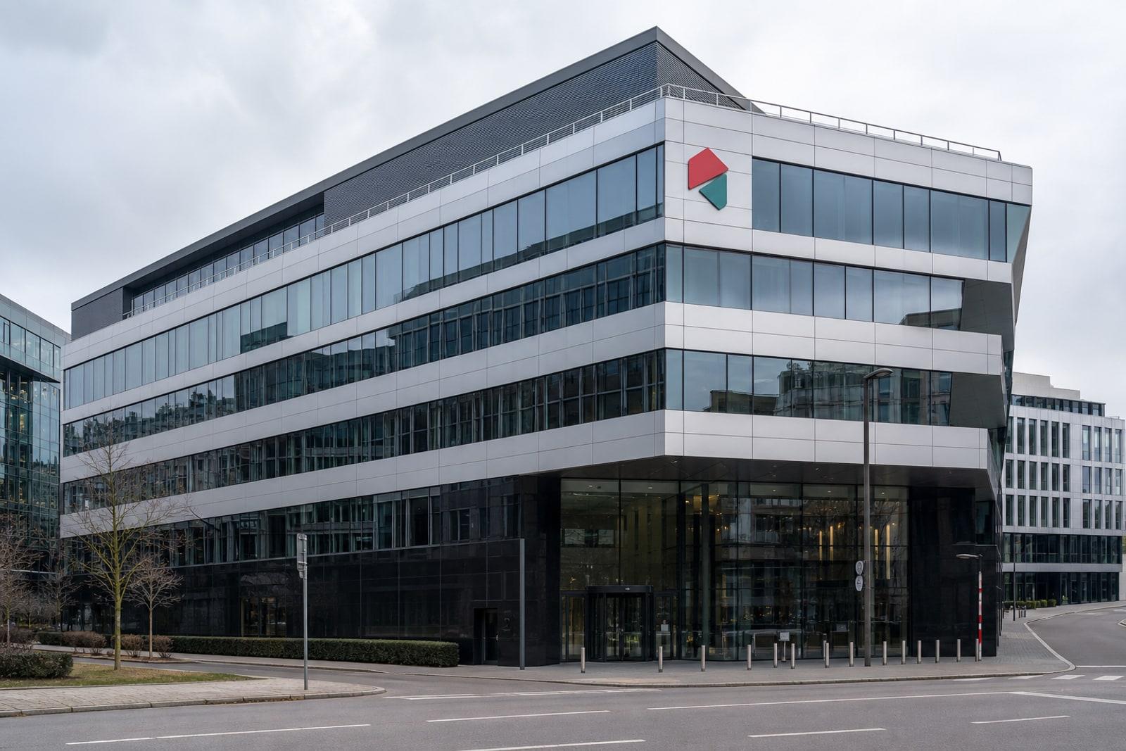 The modern glass facade of the Luxembourg Stock Exchange headquarters in Luxembourg City under an overcast sky.