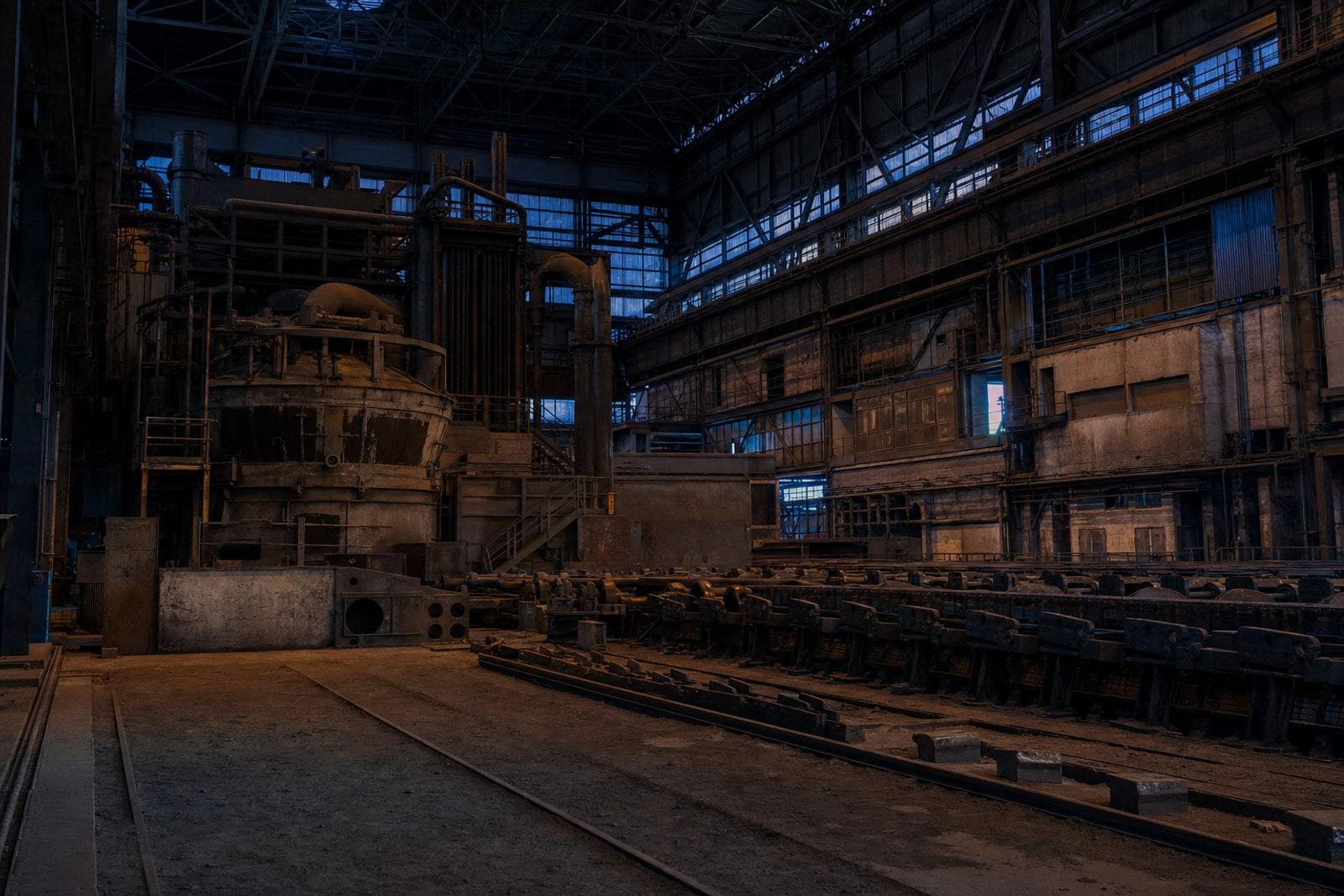 Idle electric-arc furnace hall and a still steel rolling line in a Luxembourg mill at dusk.
