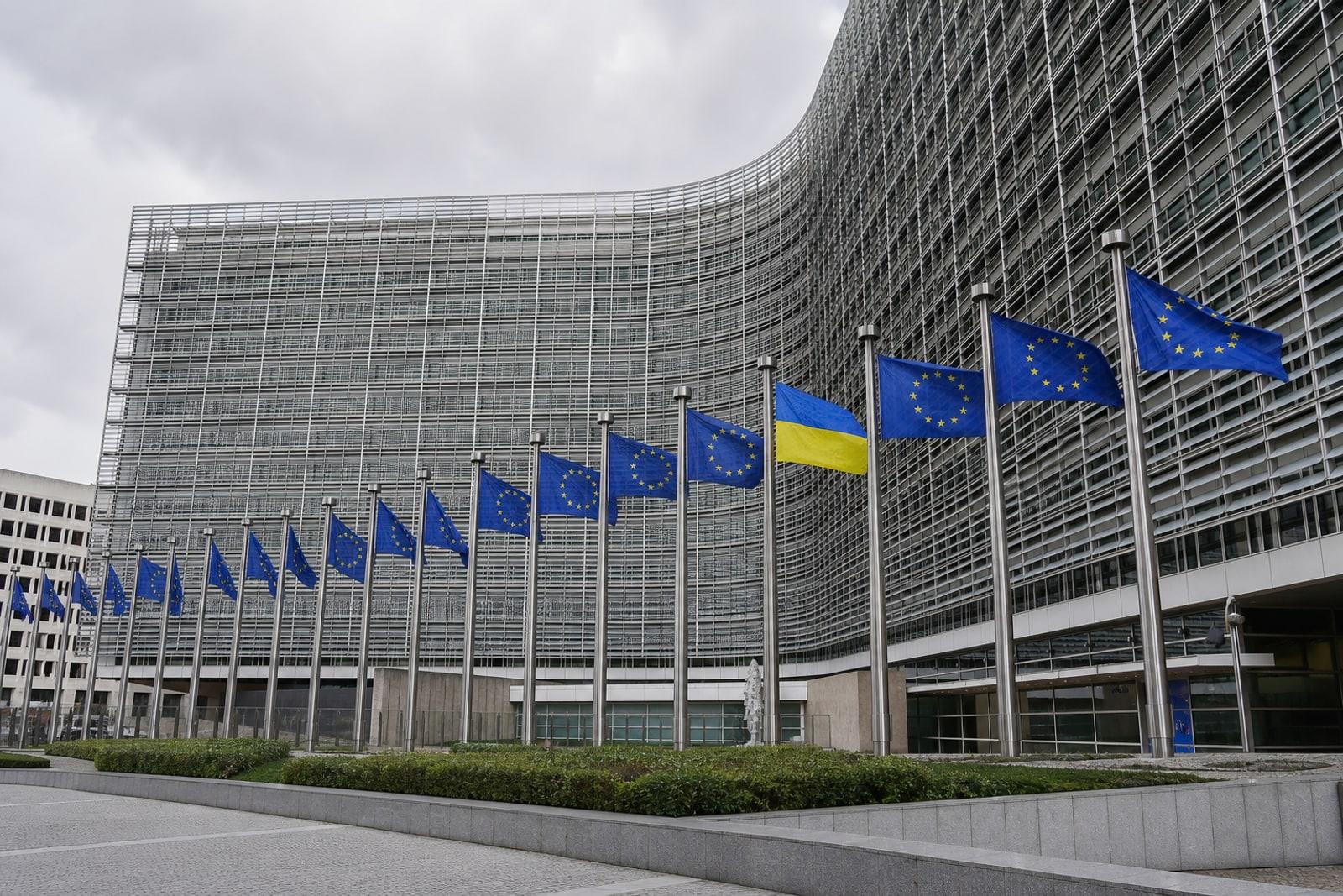 The cross-shaped glass-and-steel Berlaymont building, headquarters of the European Commission in Brussels, with European Union flags and a Ukrainian flag outside.