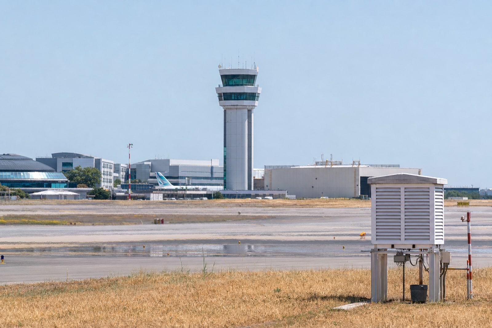Heat haze shimmers over the runway and white control tower at Luxembourg Airport in Findel under a bleached, cloudless sky.