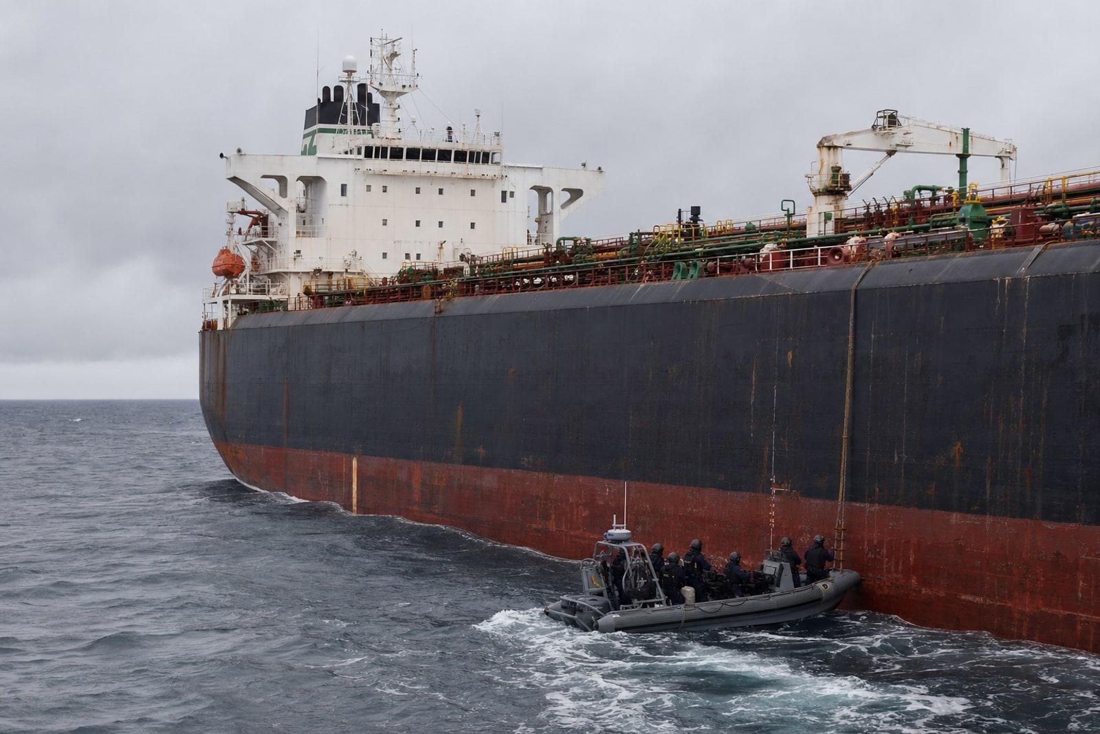 A weathered dark-hulled crude oil tanker at anchor in grey seas off the French coast with a French Navy boat approaching alongside.