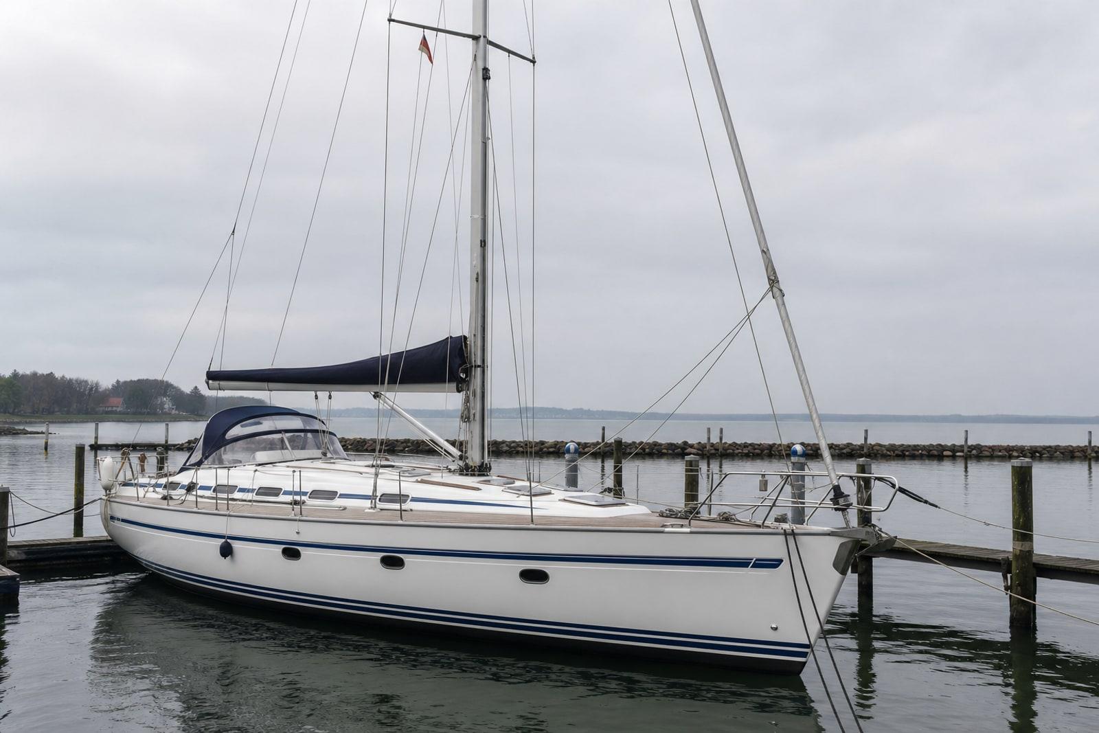 A white charter sailing yacht moored at an overcast Baltic Sea marina, its bare mast against a grey horizon.