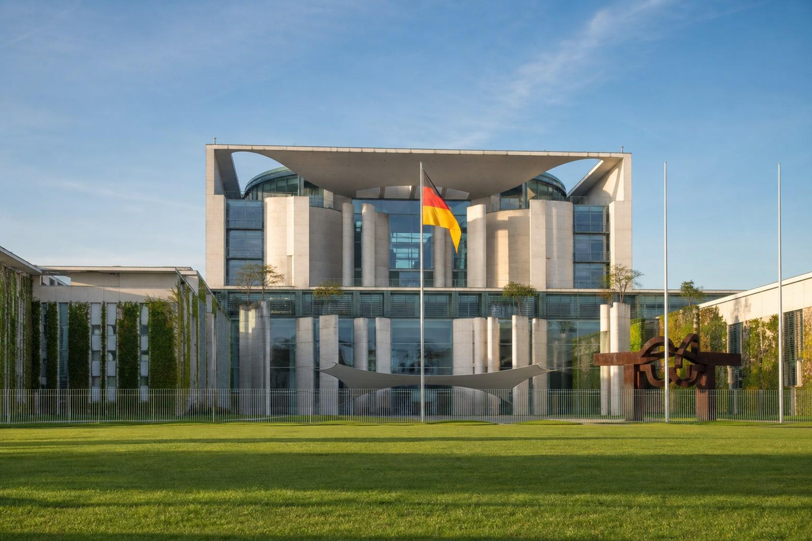 The Federal Chancellery building in Berlin, a white postmodern concrete structure with large circular façade openings, with a German flag in front
