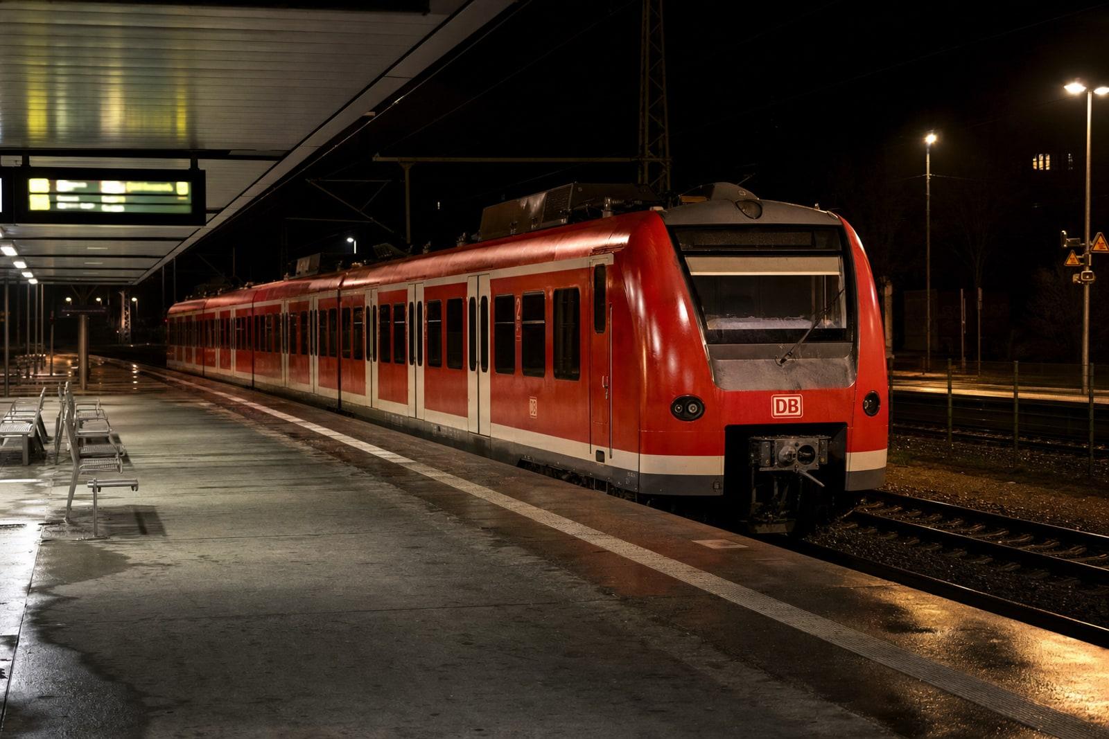 A red and white Deutsche Bahn train standing still at an empty, dimly lit German station platform at night.