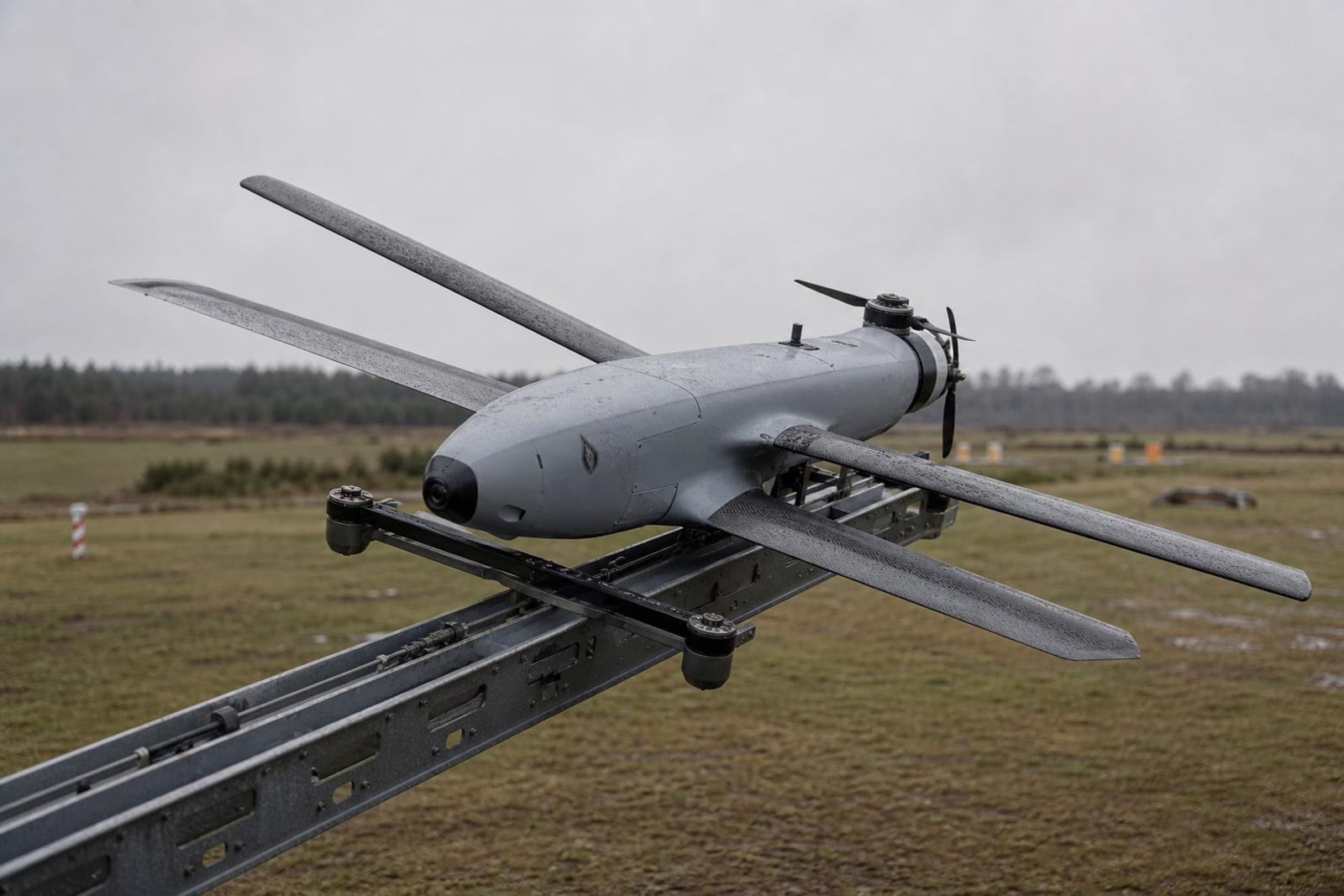 Helsing's HX-2 strike drone, a pale-grey loitering munition with X-shaped wings, on its launch rail at a test range