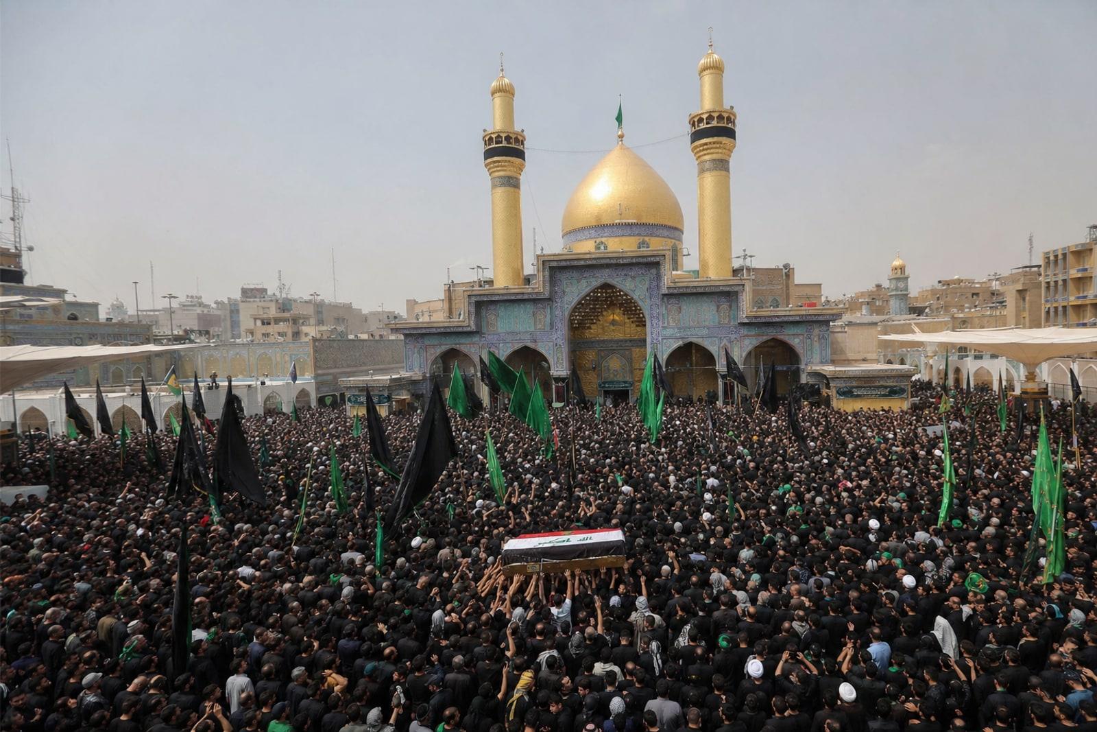Die goldene Kuppel und die Minarette des Imam-Ali-Schreins in Nadschaf, umgeben von einer riesigen Trauerprozession mit einem in eine Flagge gehüllten Sarg.