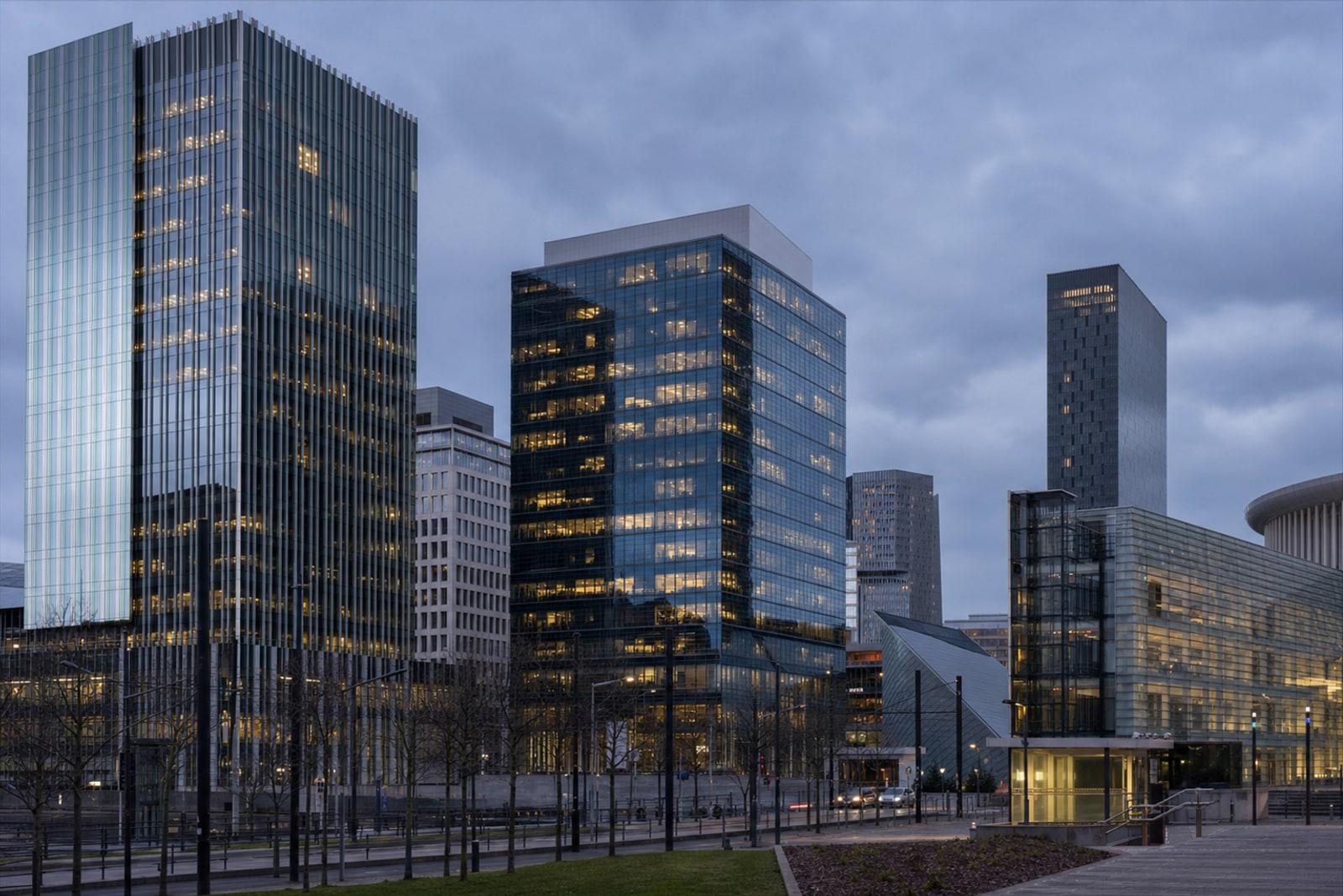 Glass office towers of Luxembourg's Kirchberg financial district at dusk under a grey-blue sky.