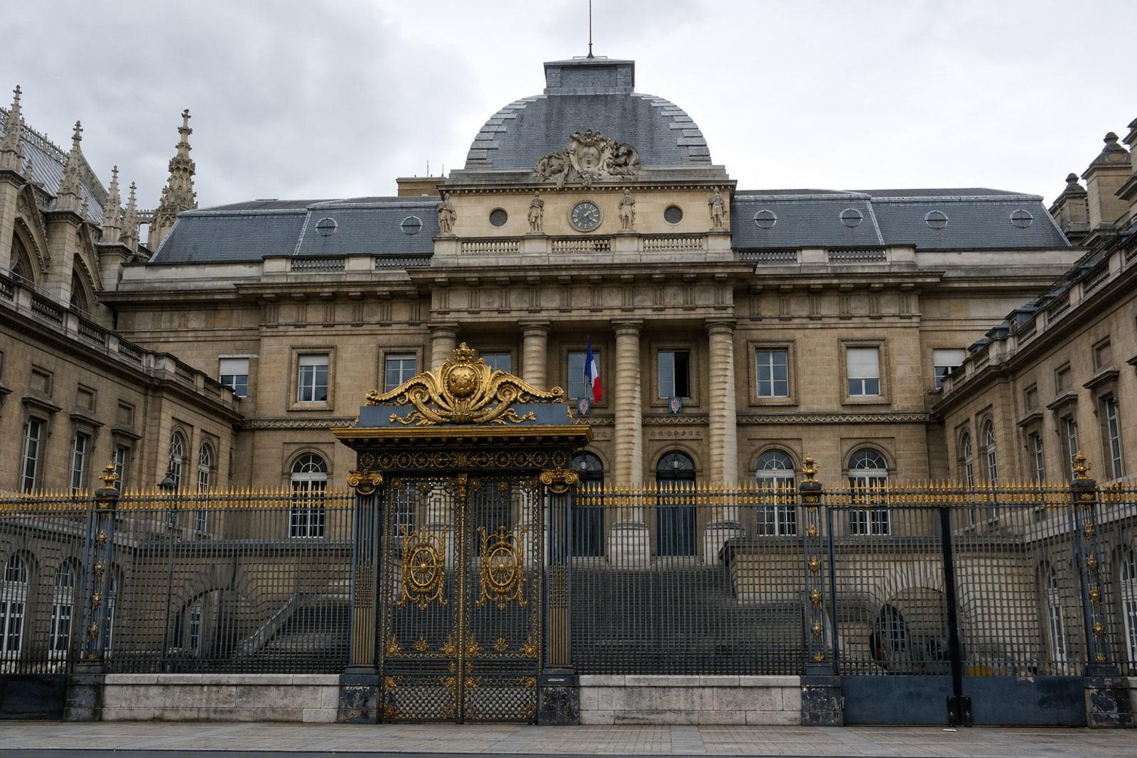 Façade monumentale en pierre grise du Palais de Justice de Paris, sur l'Île de la Cité, avec ses grilles de fer dorées.