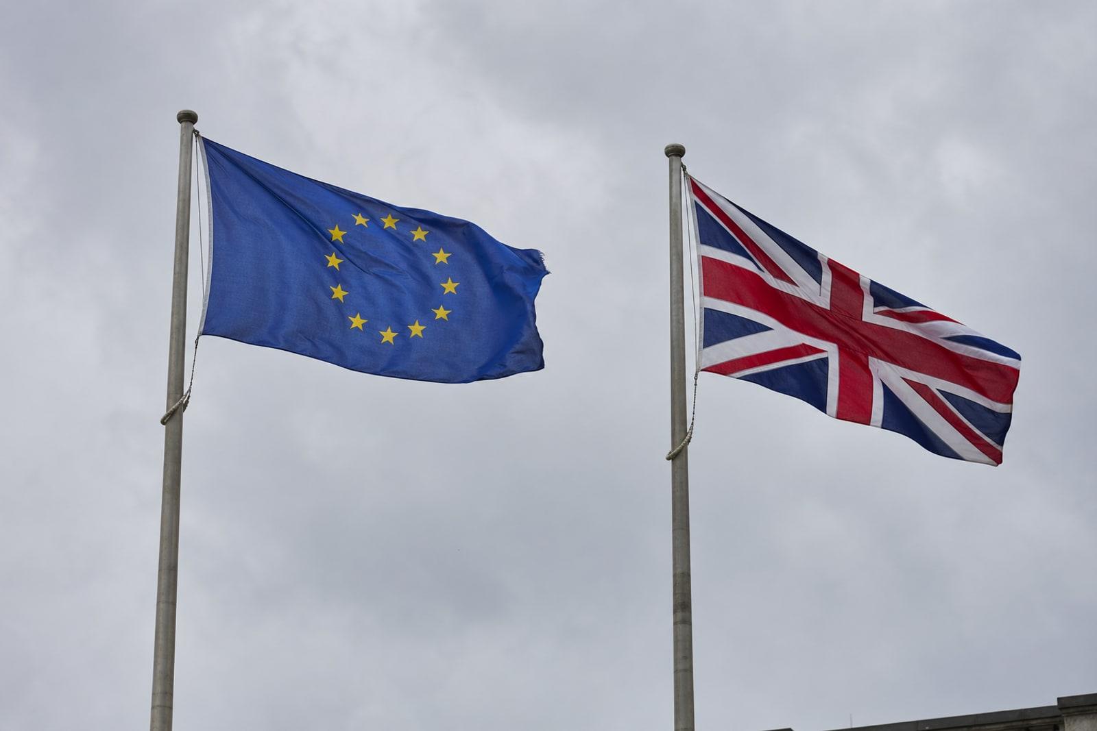 The European Union flag with its circle of twelve gold stars on blue flying beside the United Kingdom's red, white and blue Union Jack against an overcast sky.