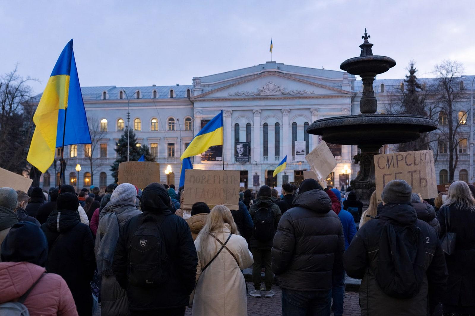 Anonymous protesters carrying Ukrainian flags and cardboard placards on Ivan Franko Square in Kyiv.