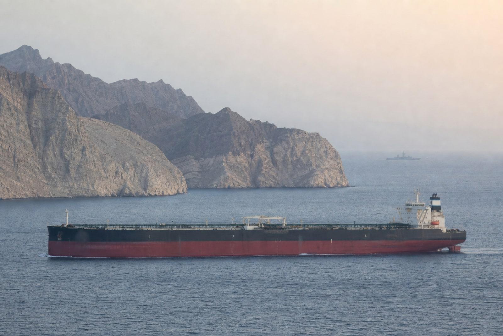 A laden crude oil tanker passes through the Strait of Hormuz, with the barren rocky headlands of Oman's Musandam peninsula behind it.