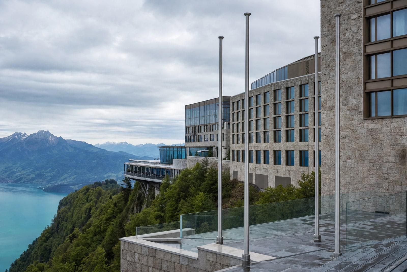 The Bürgenstock Resort's modern hotel buildings on a forested cliff high above Lake Lucerne in Switzerland under overcast light.